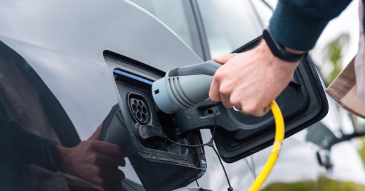 Man plugging in charger into an electric car at charge station Deduccions per vehicles electrics Llado Grup